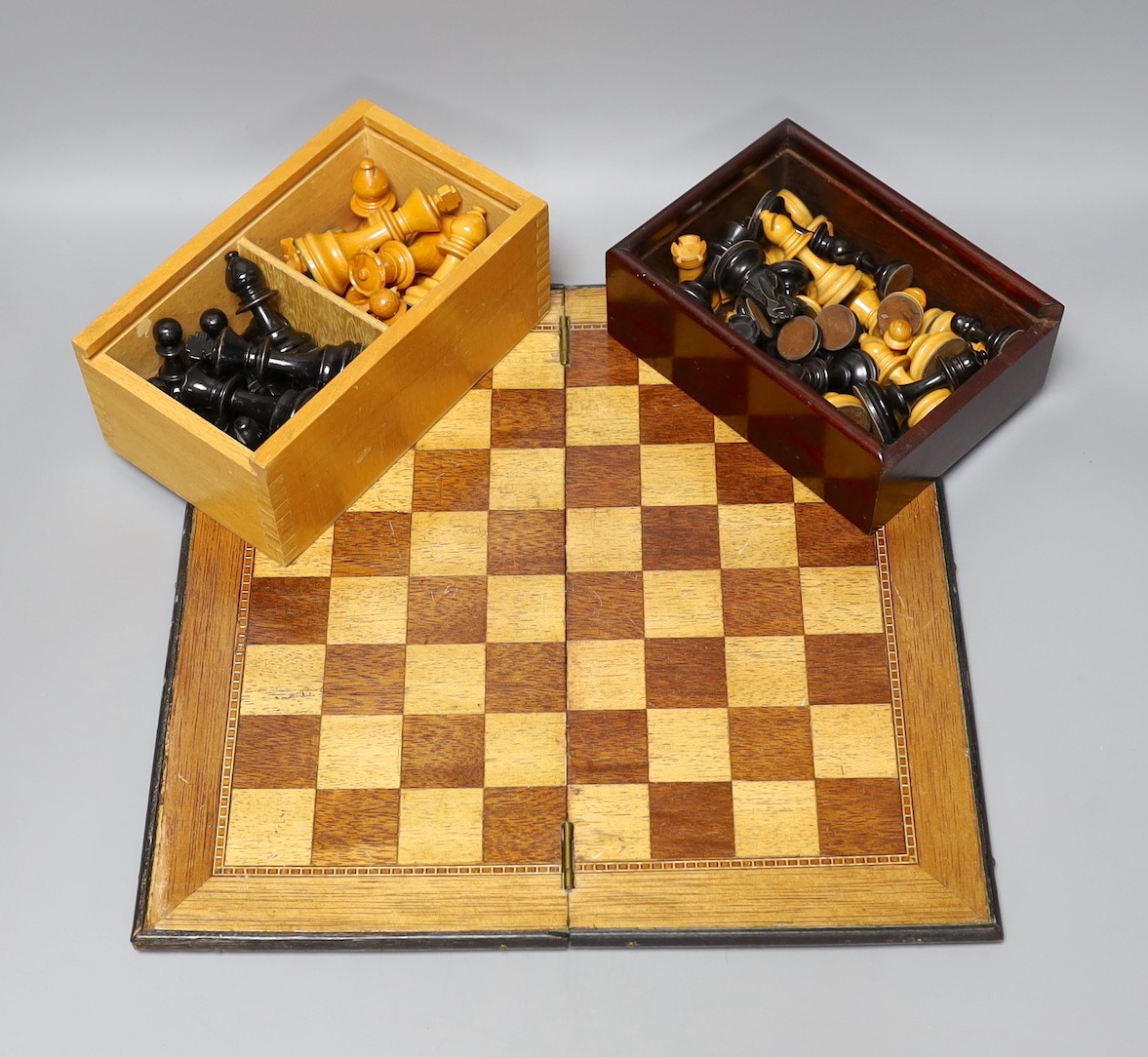 Two complete wood carved cased chess set pieces, king: 8cm and 7.5cm tall, together with a playing board